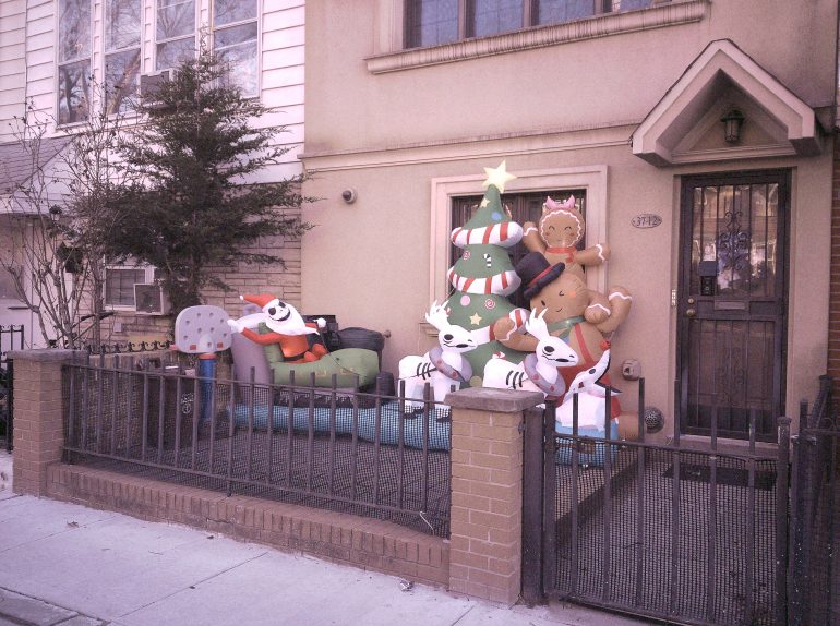 Inflatable Christmas decorations, including reindeer, Santa, and a tree, on a fenced front yard of a house.