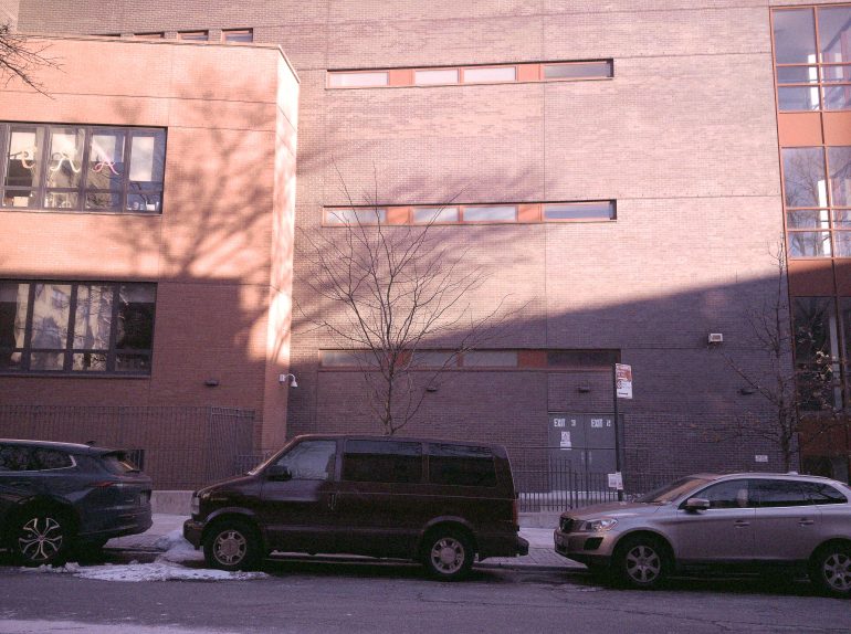 Three cars parked on a street in front of a brick building with a bare tree and snowy sidewalk.