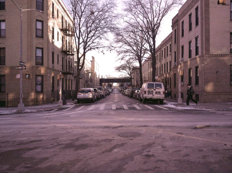 A city street lined with parked cars and brownstone buildings on a cold, winter day.
