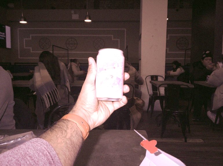 A hand holding a decorated can in a dimly lit café with people sitting at tables in the background.