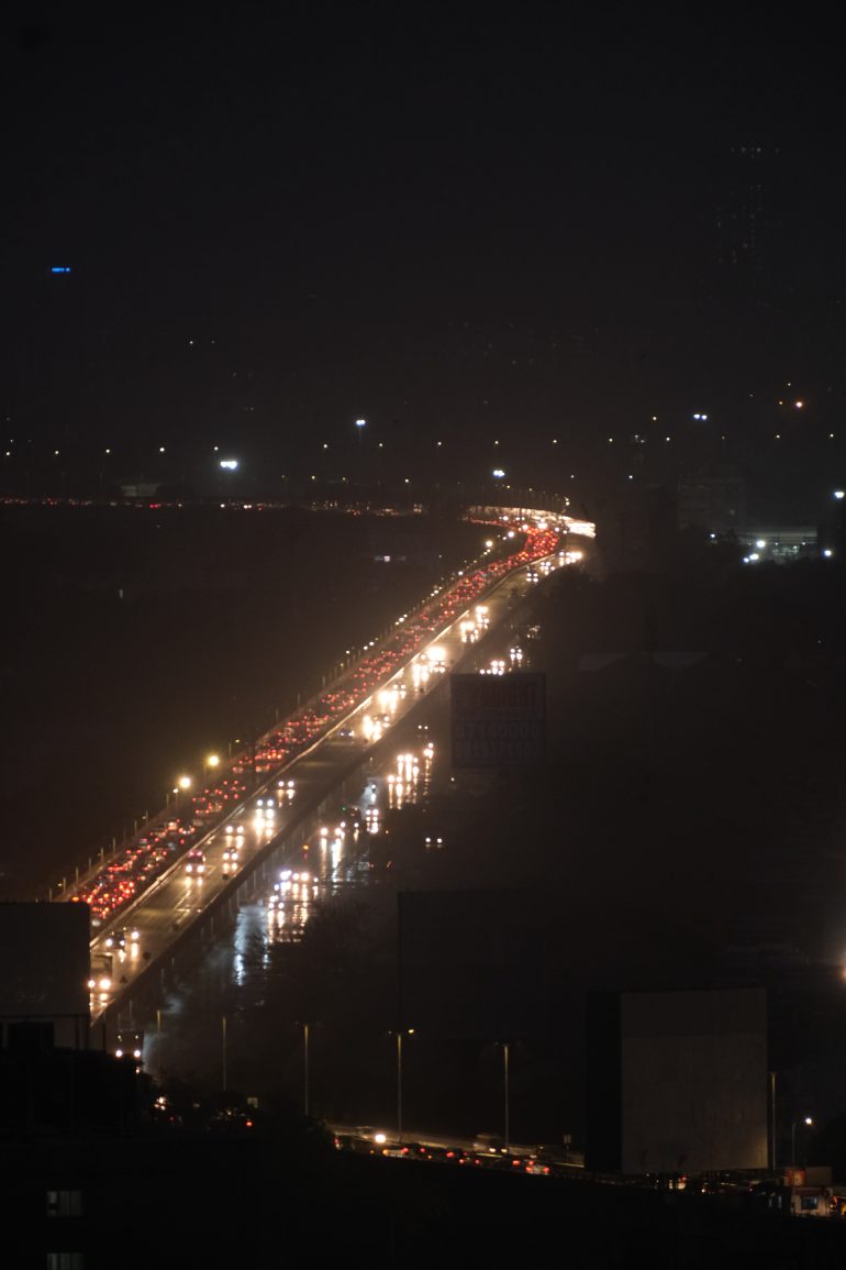 A long line of cars with headlights and taillights creates heavy traffic on a city highway at night.