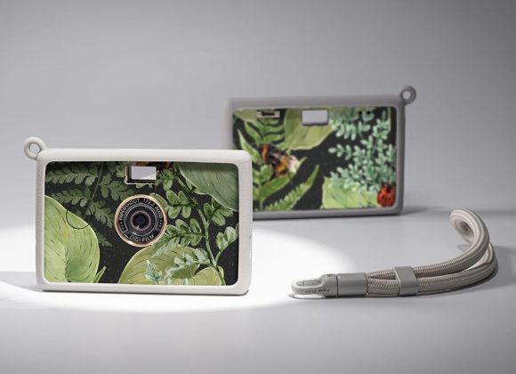 Two compact cameras with leafy green and nature-themed designs and white frames, on a grey background.