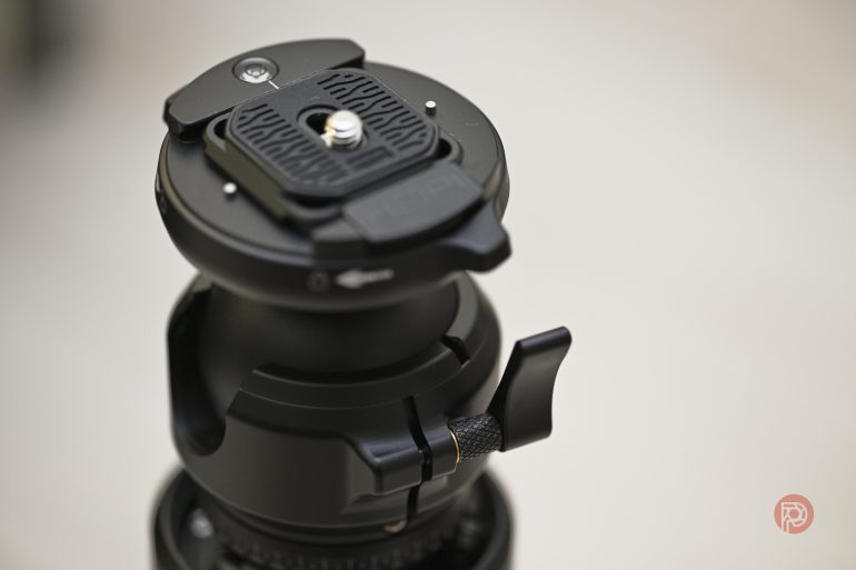 Close-up of a black camera tripod ball head with adjustment knobs and textured quick-release plate.