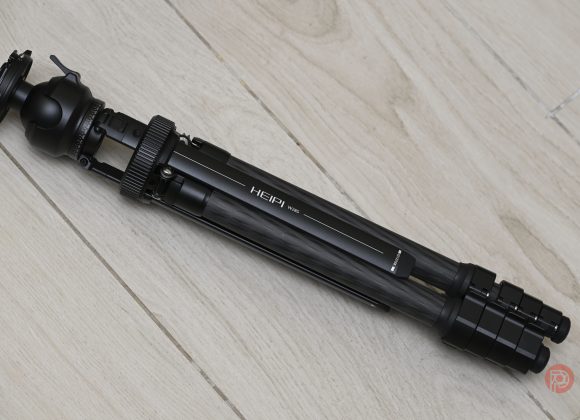 A folded black tripod labeled HEIPI 105 lying on a light wooden floor.