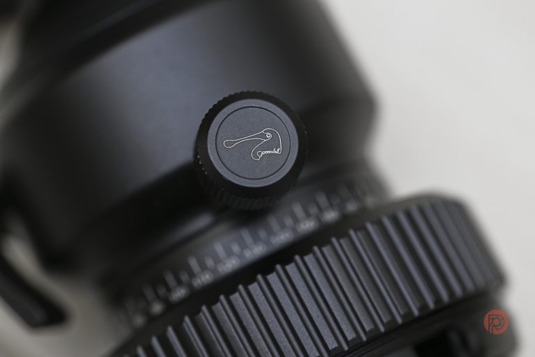 Close-up of a camera lens adjustment knob with a logo and gear-like focus ring in view.