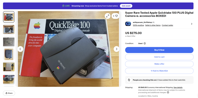 Apple QuickTake 100 digital camera with accessories, box, and manual displayed on a table for sale online.