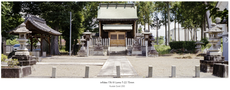 A small Japanese shrine with stone lanterns and trees, viewed from the front on a sunny day.