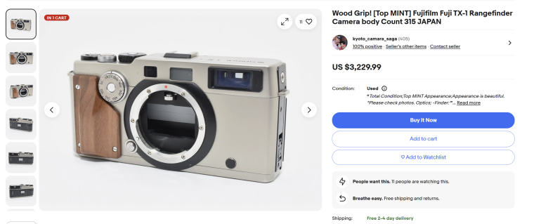 A silver Fujifilm TX-1 rangefinder camera with a wood grip, shown without a lens attached.