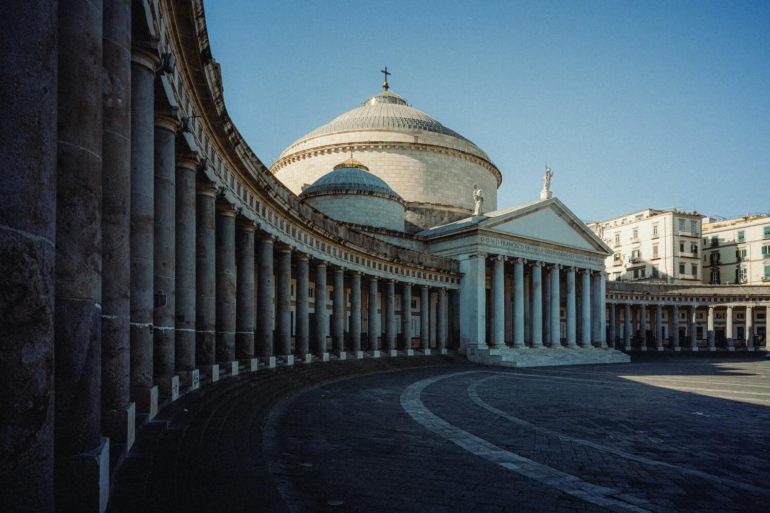 Large neoclassical church with a dome, columns, and statues in a spacious, sunlit square.