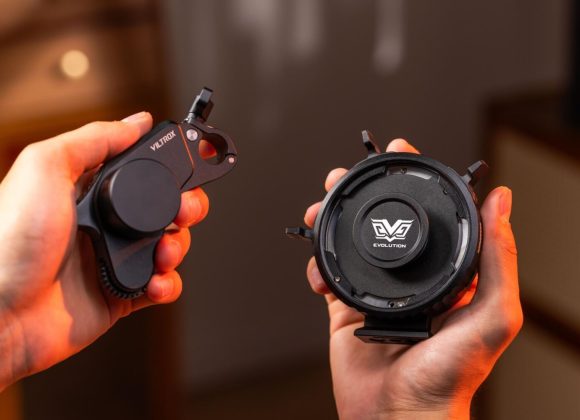 Two hands hold camera lens accessories with Viltrox and Evolution logos, against a warm blurred background.