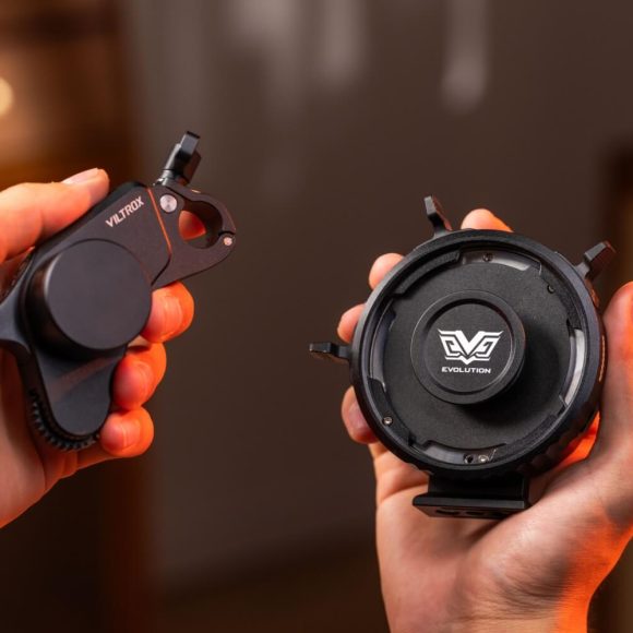Two hands hold camera lens accessories with Viltrox and Evolution logos, against a warm blurred background.
