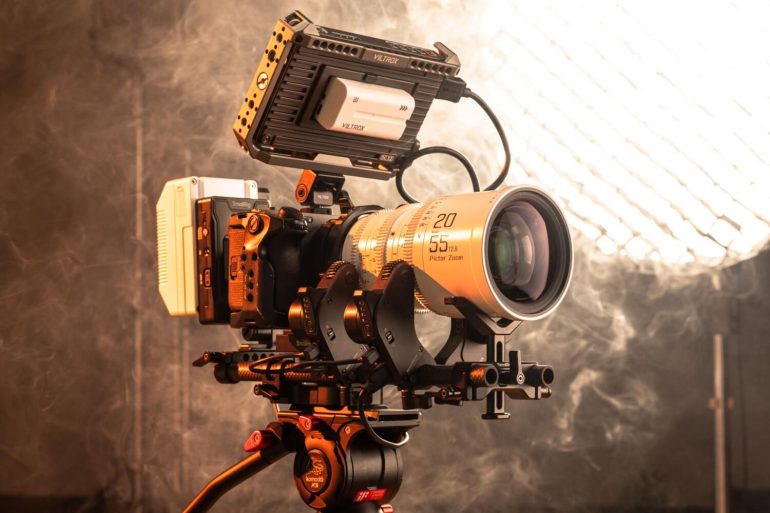 Professional cinema camera with a large zoom lens and monitor setup on a tripod in a smoky studio environment.