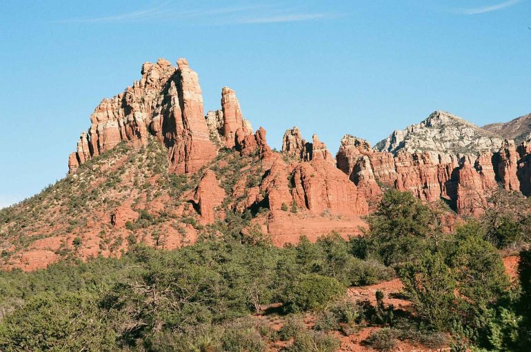 Red rock formations and green shrubs under a clear blue sky in Sedona, Arizona.