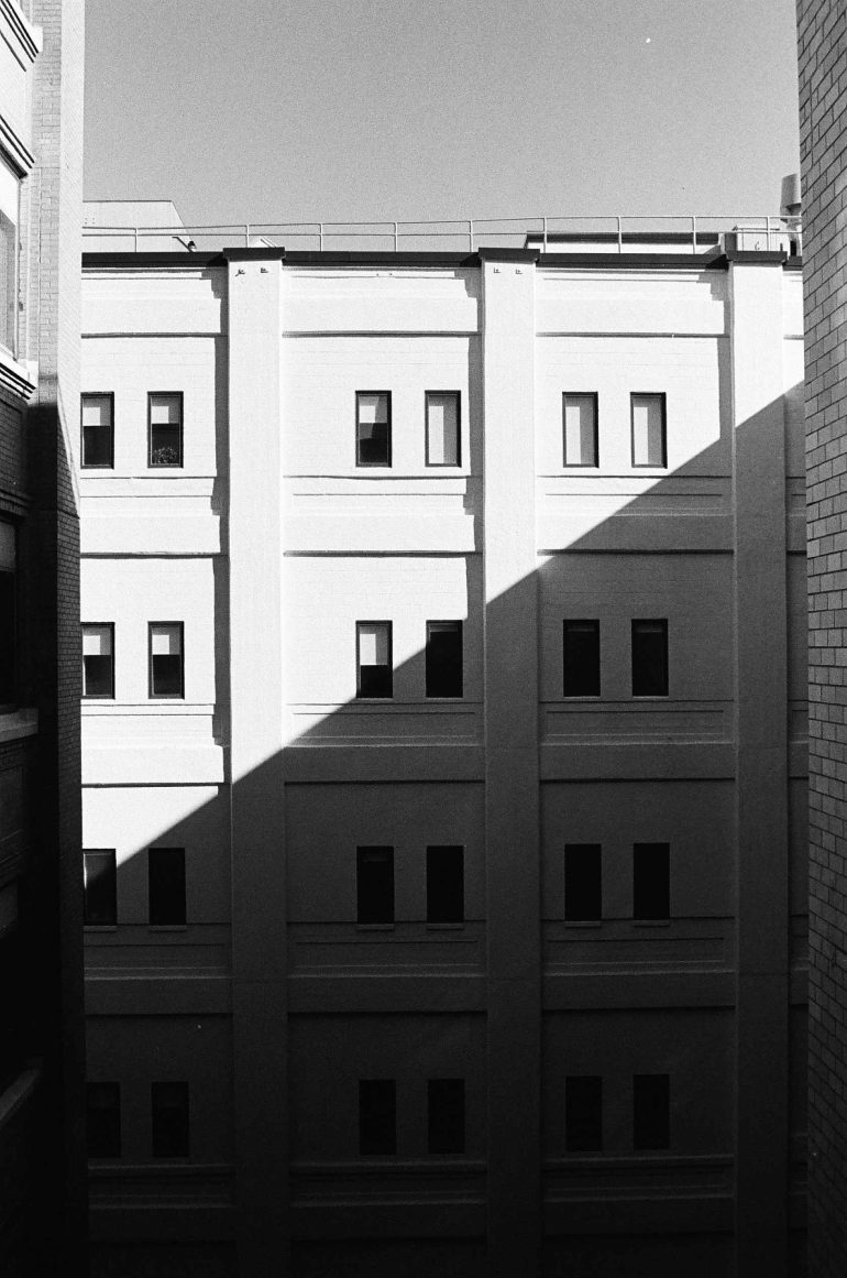 Black and white photo of a building facade with windows, half in sunlight and half in shadow.