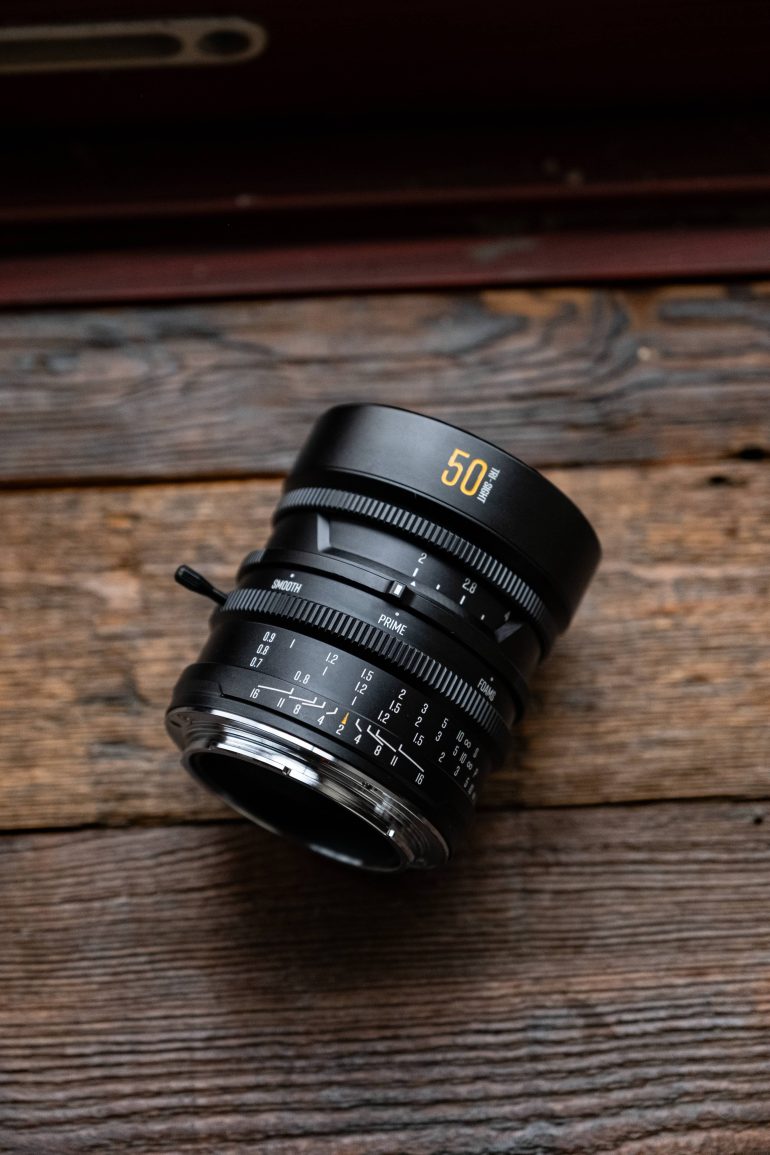 A black 50mm camera lens rests on a rustic wooden surface.