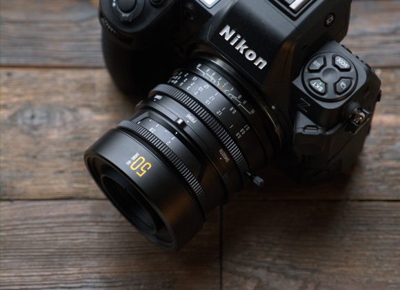 A Nikon camera with a 50mm lens rests on a wooden surface near a window.