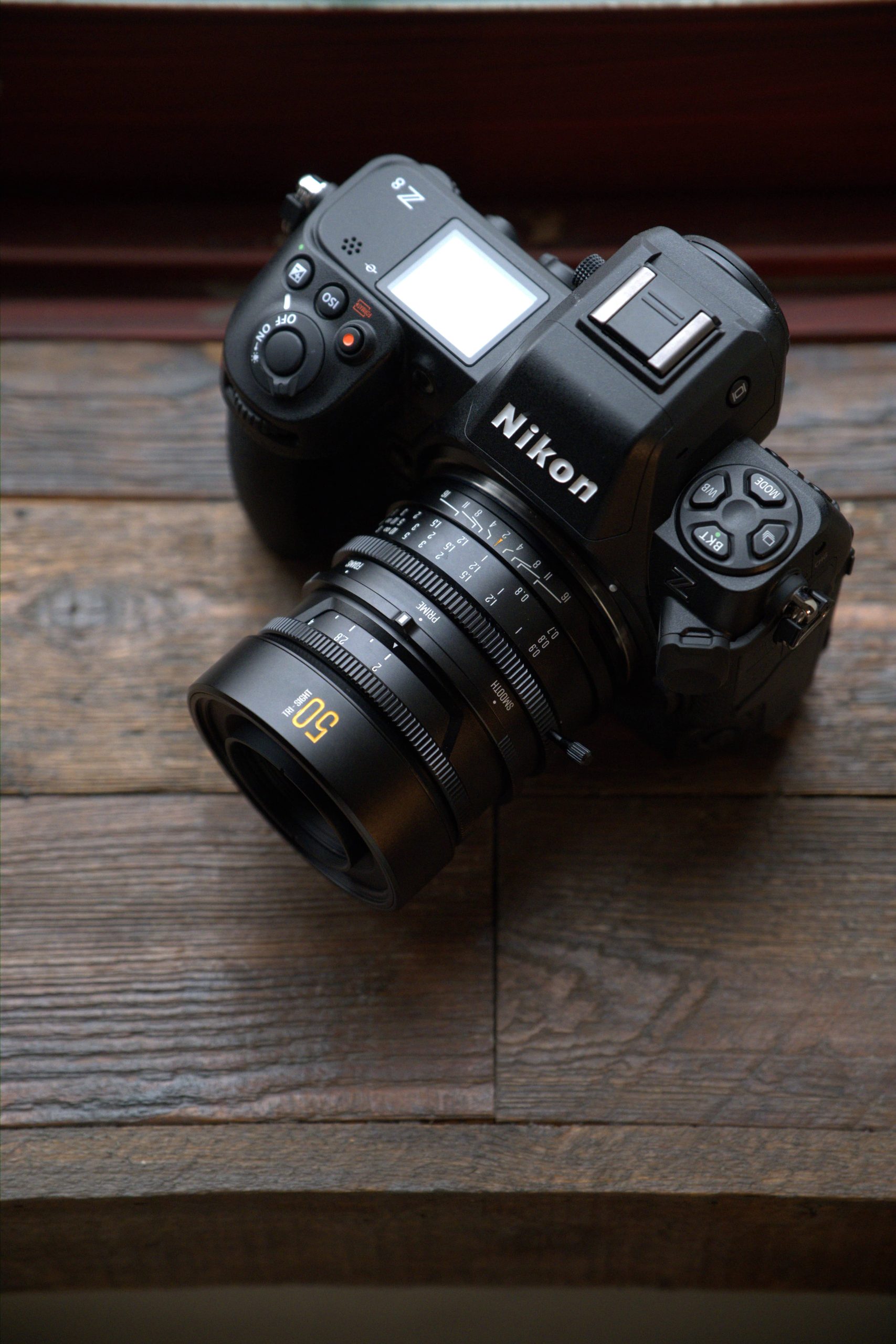 The Two Awesome Announcements from Brightin Star at CP+ 2026 A Nikon camera with a 50mm lens rests on a wooden surface near a window.
