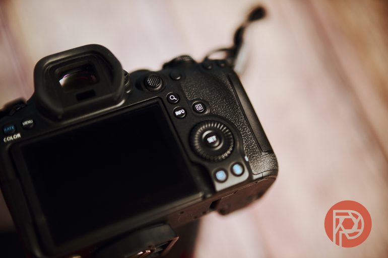 Close-up of a DSLR camera’s back with a blurred background and a red circular logo in the lower right corner.