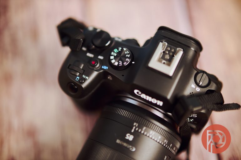 Top view of a Canon camera with lens, showing mode dial and controls on a blurred wooden surface.