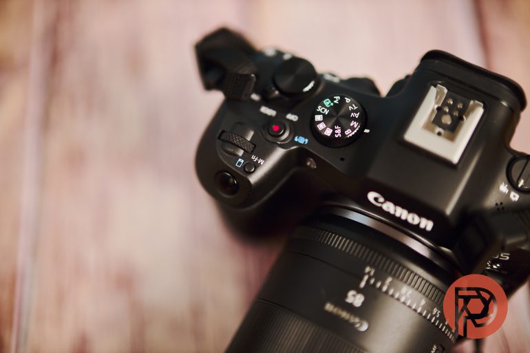 Close-up of a Canon camera with visible mode dial, resting on a wooden surface.