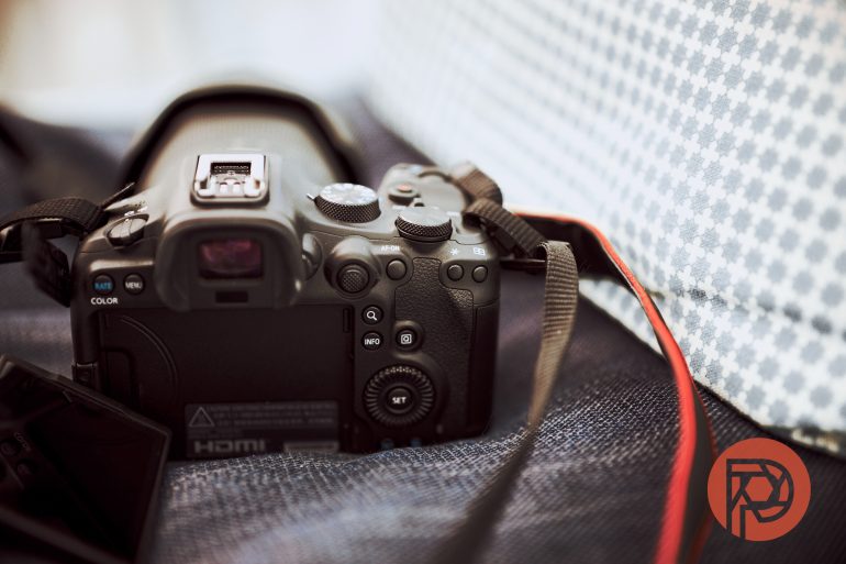A DSLR camera with a red strap rests on a soft, textured surface next to a patterned background.