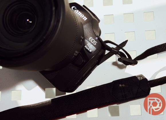 Close-up of a Canon EOS R6 Mark II camera on a white, perforated surface with a black camera strap.