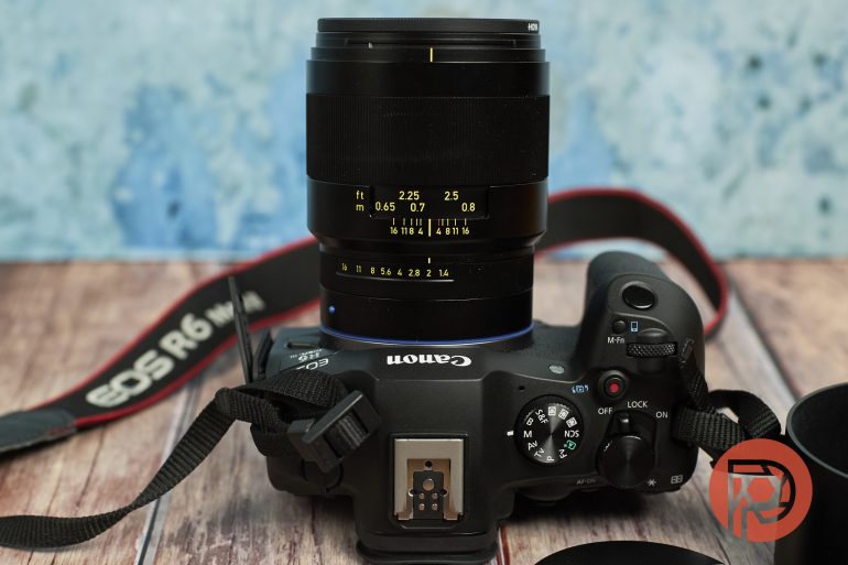 Canon EOS R6 camera with a black lens on a wooden surface, camera strap visible, and blue background.