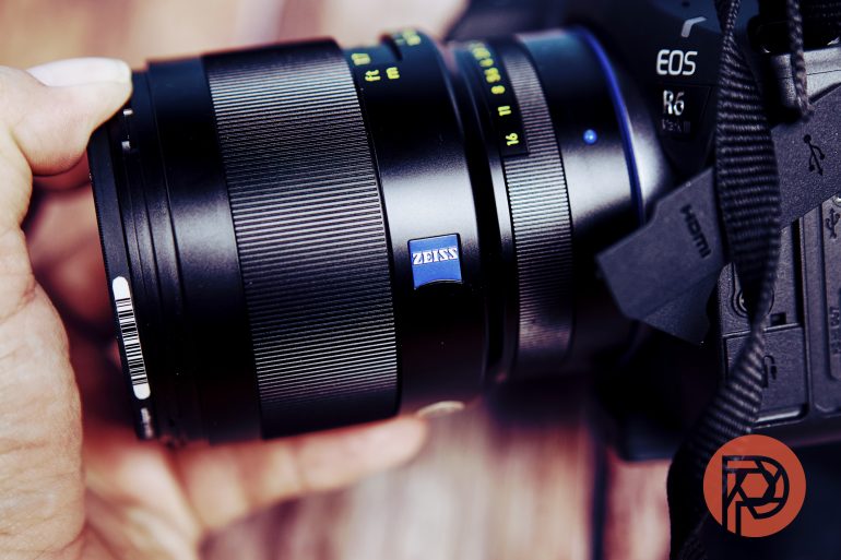 Close-up of a hand holding a camera with a Zeiss lens, showing brand name and lens details.