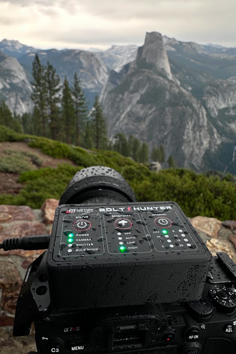 A camera with raindrops on it faces Half Dome in Yosemite National Park on a cloudy day.