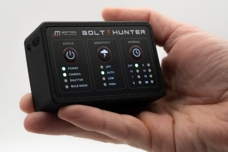 A hand holding a black Bolt Hunter device with lit status and sensitivity indicator lights.