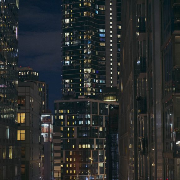Night cityscape showing tall, glass buildings with many lit windows against a dark sky.