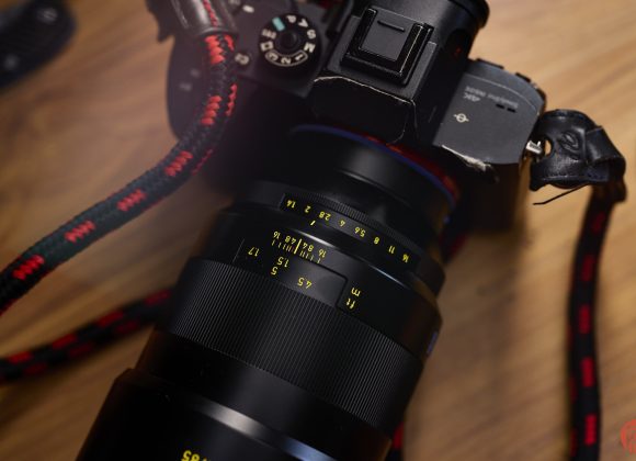 Close-up of a camera with a zoom lens, focused on the lens markings and numbers, on a wooden surface.