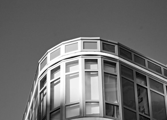 Modern glass building corner against a clear sky, with sunlight reflecting on the windows.