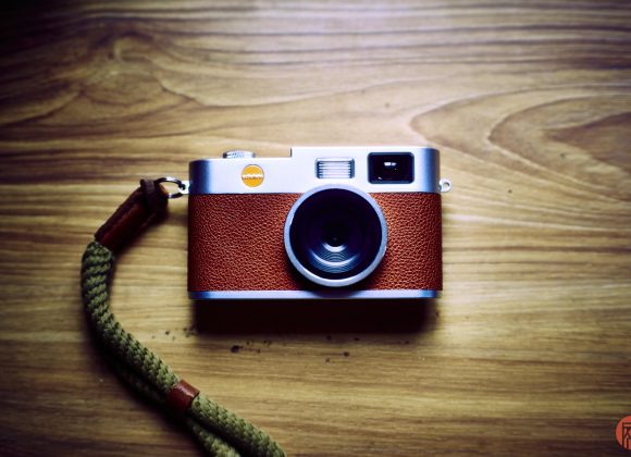 A vintage-style camera with a brown leather grip and green strap on a wooden surface.