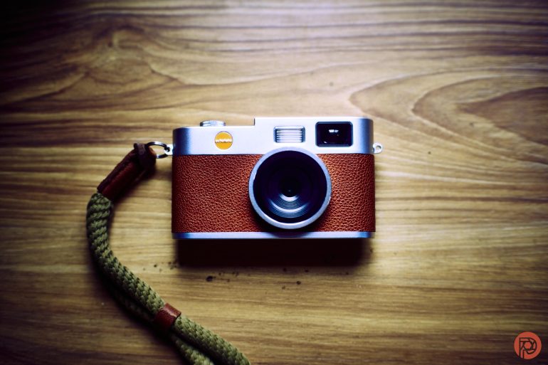 A vintage-style camera with a brown leather grip and green strap on a wooden surface.