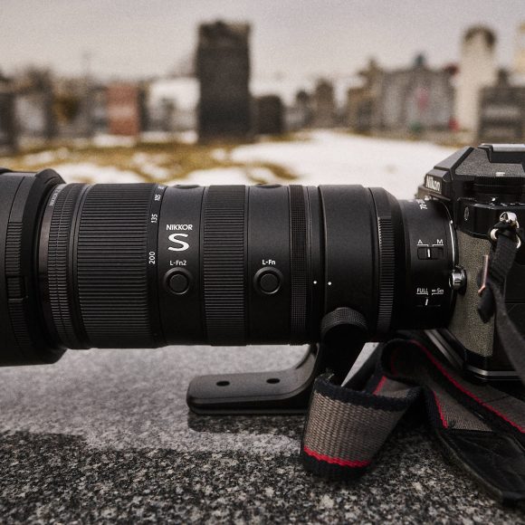 A black DSLR camera with a large telephoto lens sits on a stone surface in a cemetery.