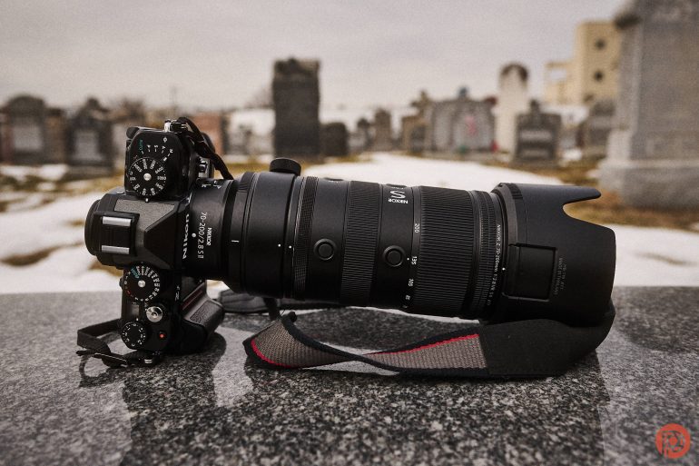 A black DSLR camera with a large telephoto lens rests on a stone surface in a cemetery.