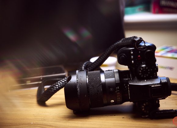 A DSLR camera with a zoom lens and strap sits on a wooden table in soft lighting.
