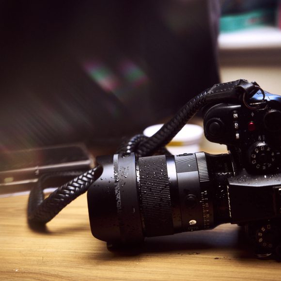 A DSLR camera with a zoom lens and strap sits on a wooden table in soft lighting.