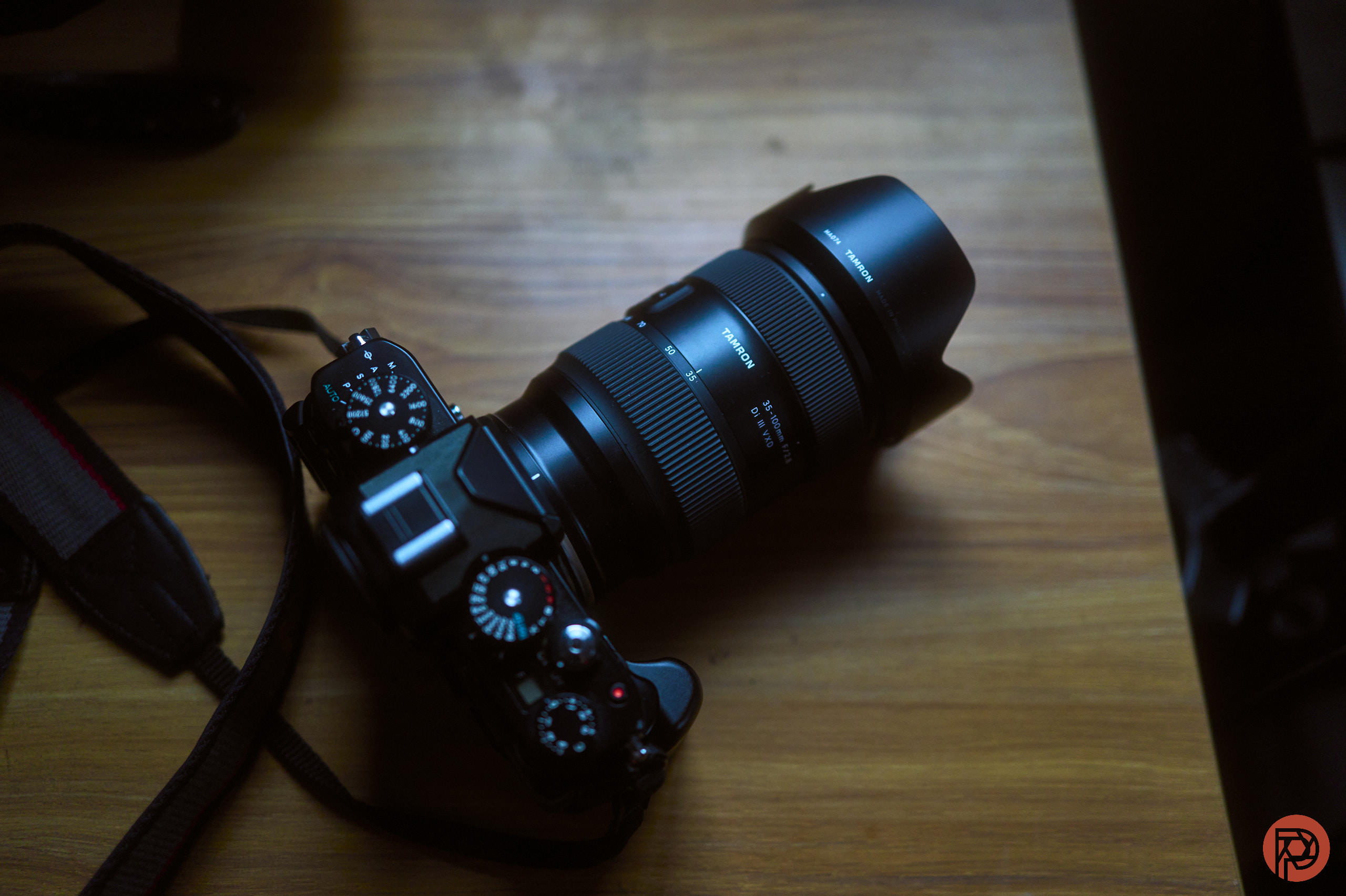 A black DSLR camera with a zoom lens sits on a wooden surface in dim lighting.