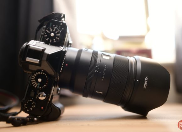 A black digital camera with a Viltrox lens rests on a wooden surface in soft natural light.