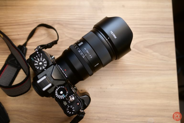 A black digital camera with a Viltrox lens rests on a wooden surface.