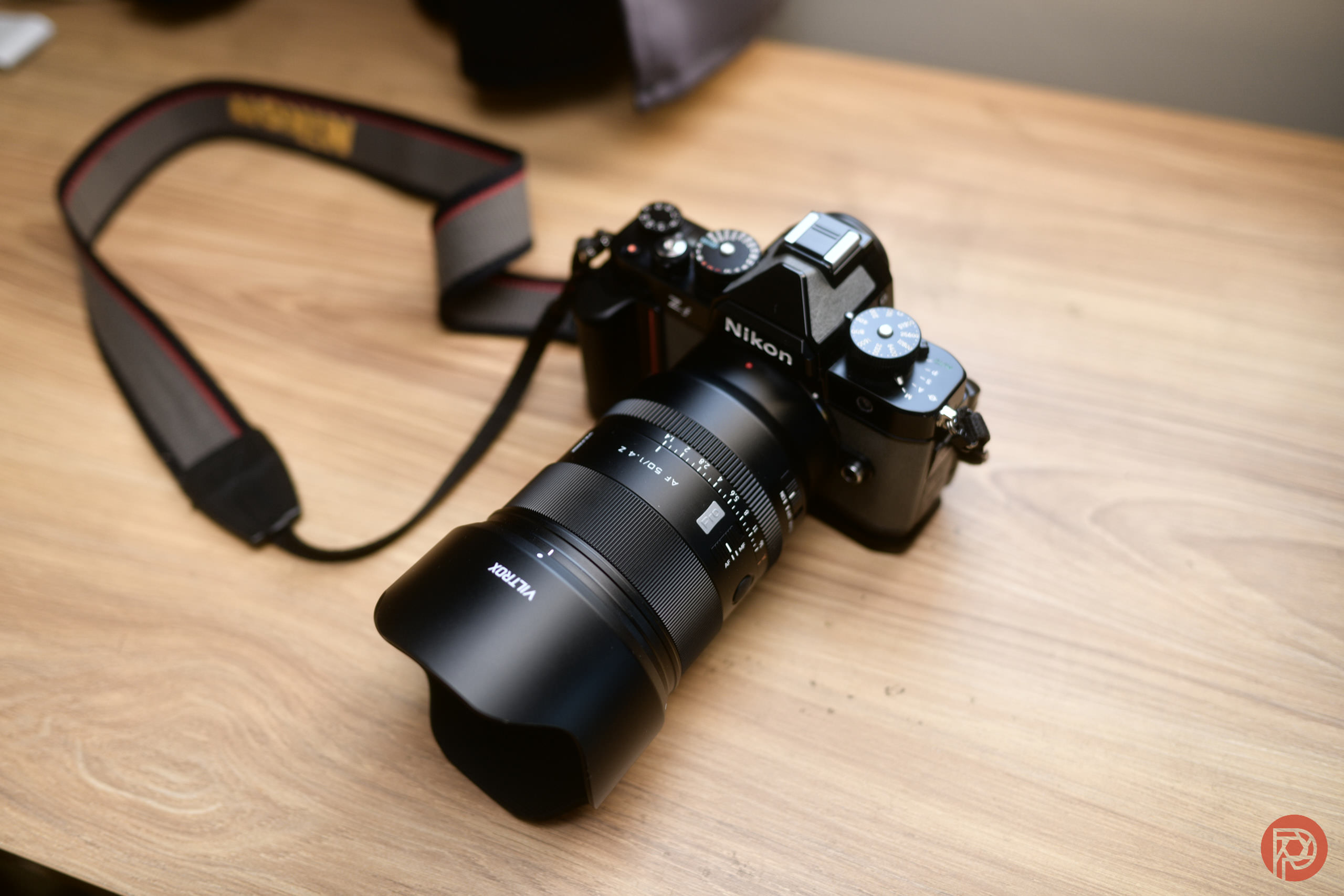 A Nikon camera with a large lens sits on a wooden surface with its strap attached.