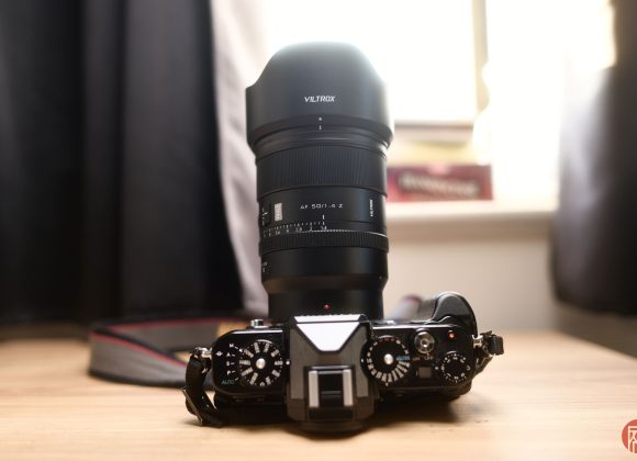 A Viltrox camera lens attached to a camera, resting on a wooden surface with blurred background.