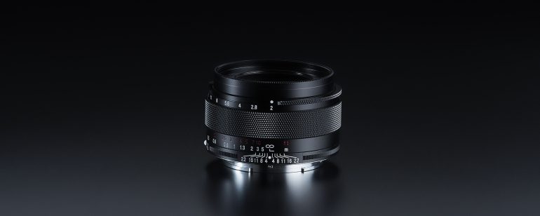 A black camera lens with focus and aperture markings, placed on a reflective dark surface.