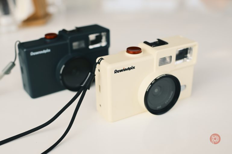Two compact Rewindpix cameras, one black and one cream, with wrist straps on a white surface.