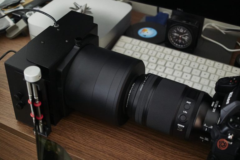 A close-up of a large camera setup with a lens and accessories on a desk beside a computer keyboard.