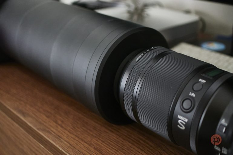 Close-up of a large camera lens with controls, resting on a wooden surface near a keyboard.