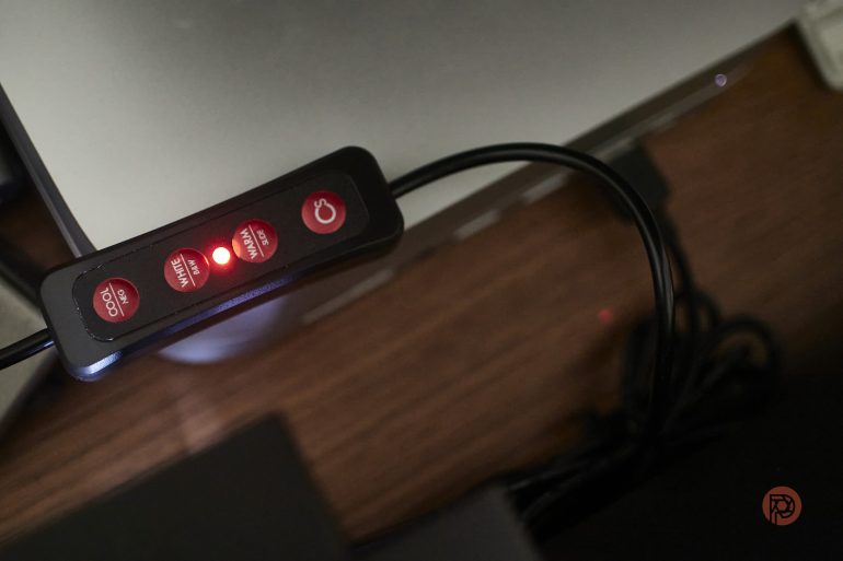 Close-up of a black remote control with red buttons and a glowing red LED indicator, on a wooden surface.