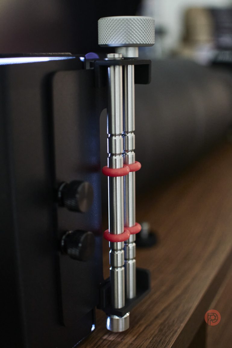 Close-up of a metal rod with three red rings, attached to a black device on a wooden surface.